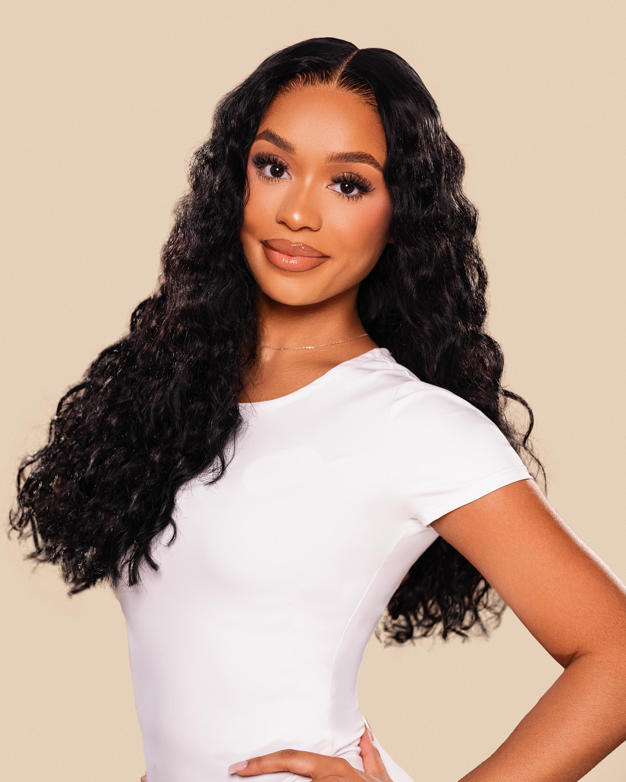 Woman with long, wavy hair wearing a white top against a beige background