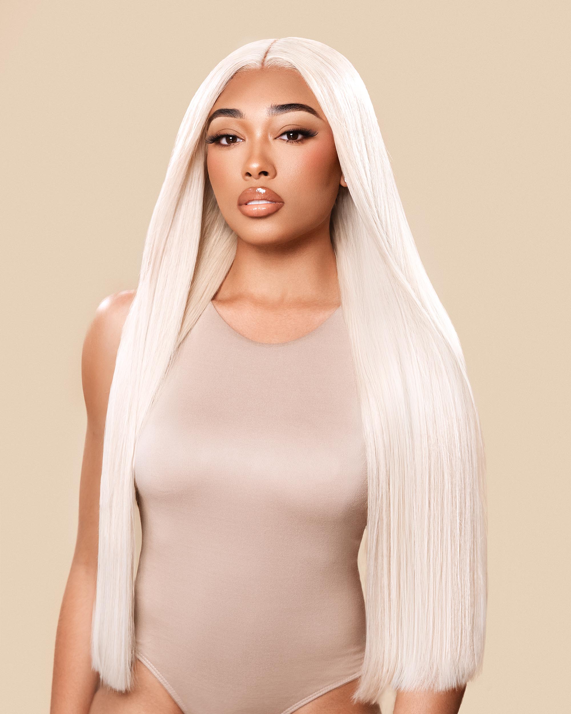 Woman wearing a beige bodysuit with a long blonde wig on a beige background