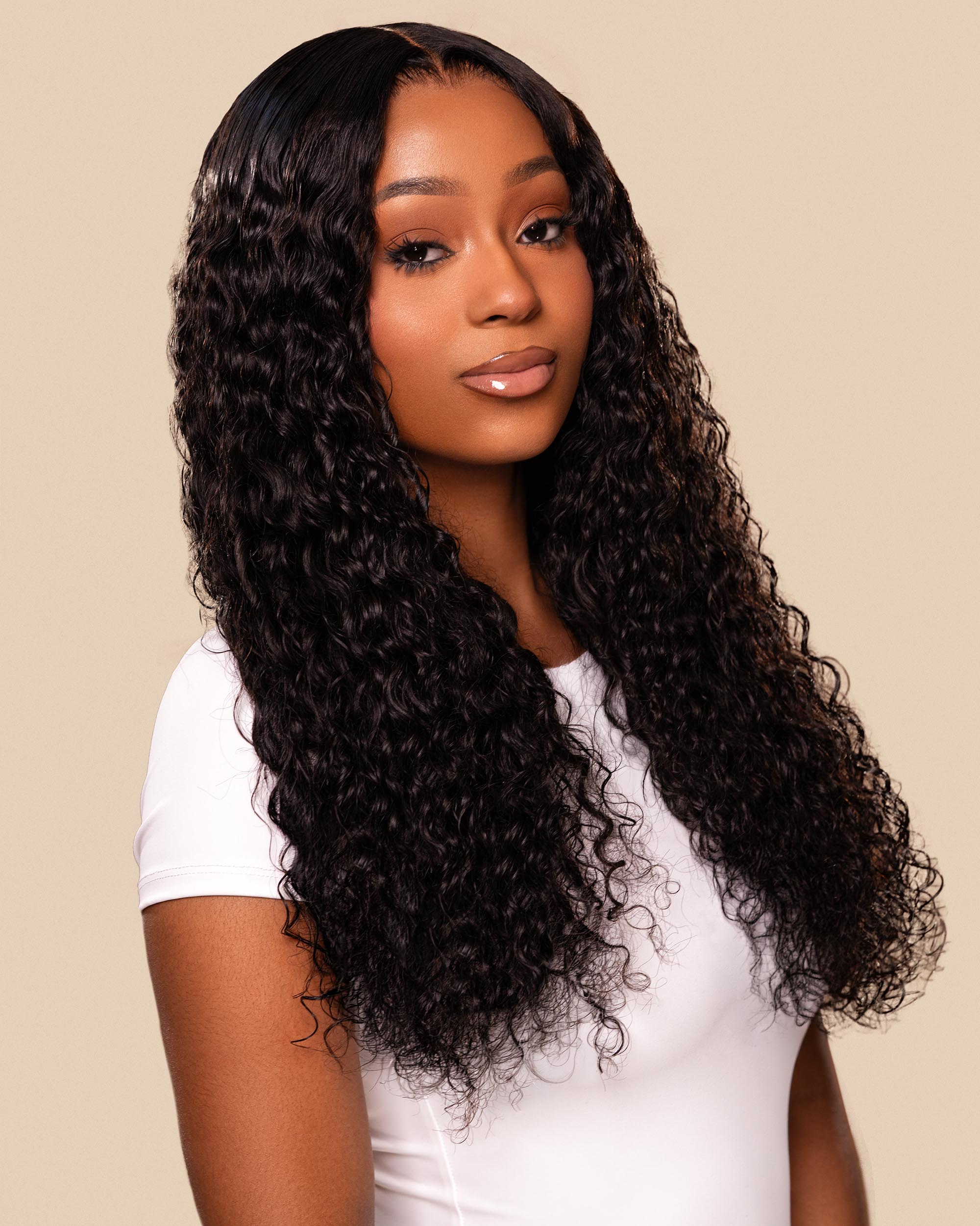 Woman with long, curly black hair wearing a white top on a beige background